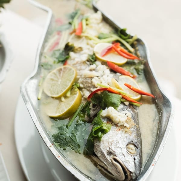 Steamed whole fish with lime, chilies, and herbs in a silver serving dish.