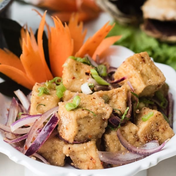 Crispy fried tofu with red onions, green onions, and chili flakes, garnished with carved carrots.
