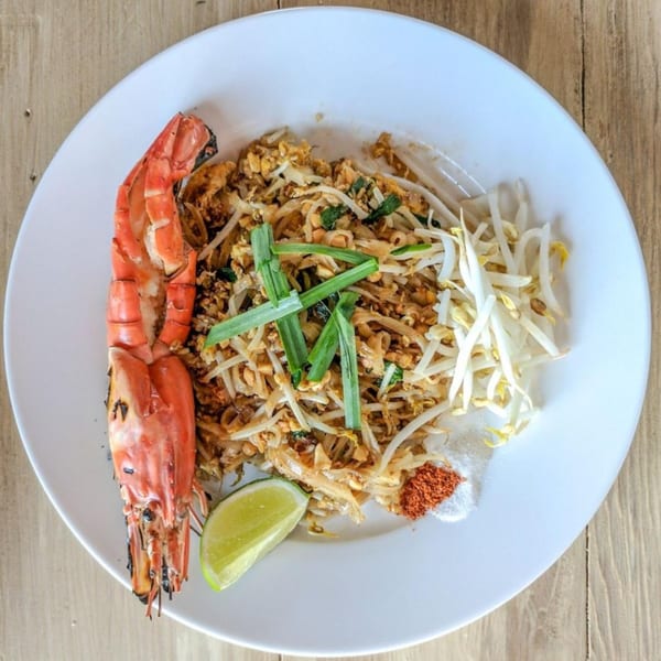 Subhannahong Royal Thai Cuisine's Pad Thai with a large grilled prawn, lime, and spices on a white plate.